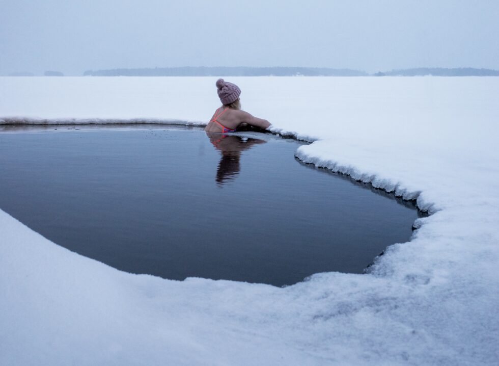 A swimmer shoulder deep in a hole cut through lake ice
